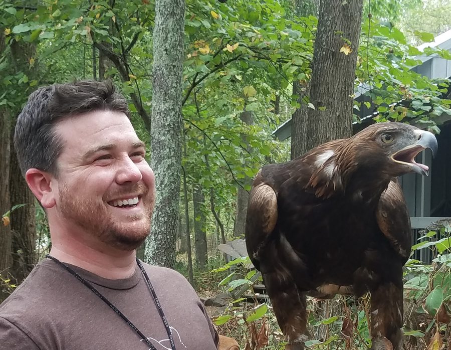 Taylor Berry laughing beside a golden eagle perched on his gloved hand